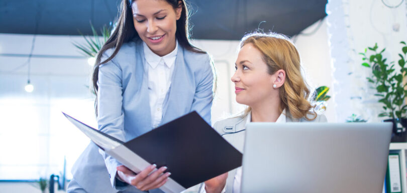 business woman showing paper documents her older female colleague office