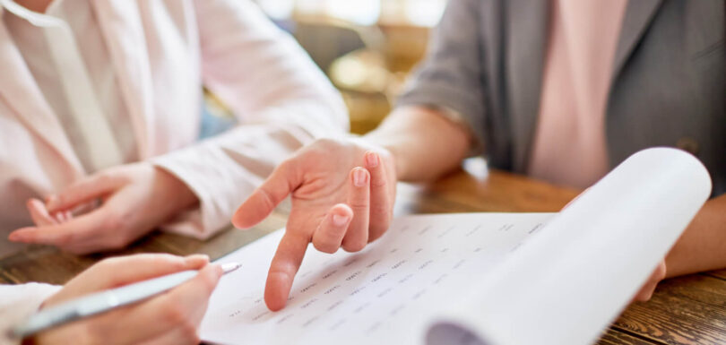 Dwie kobiety przeglądające dokumenty. Jedna z nich wskazuje palcem na kartkę, a druga trzyma długopis, gotowa do pisania. Temat: Skala semantyczna - jak ją skutecznie wykorzystać w kwestionariuszu ankiety?