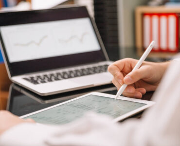 Osoba korzystająca z tabletu i laptopa do analizy danych i planowania strategii biznesowej, symbolizująca płatne badania rynku online i podejmowanie świadomych decyzji.