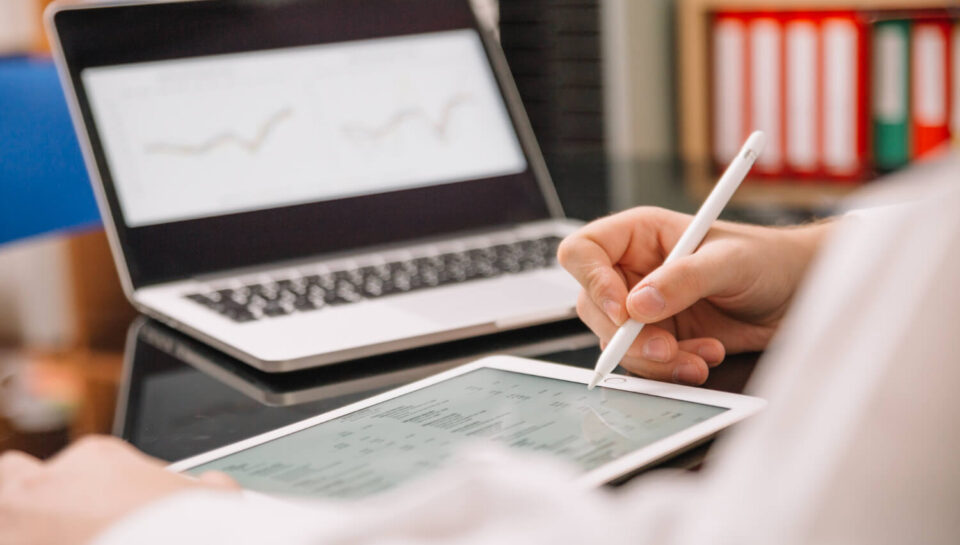 Osoba korzystająca z tabletu i laptopa do analizy danych i planowania strategii biznesowej, symbolizująca płatne badania rynku online i podejmowanie świadomych decyzji.