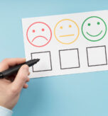 Dłoń trzymająca pisak nad ankietą satysfakcji, przygotowująca się do zaznaczenia opcji z czerwoną, smutną buźką. Temat: Wskaźnik Churn Rate