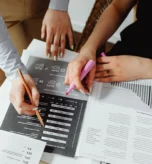 Dwie osoby analizują wydruk wyników ankiety pracowniczej z procentami i wykresem kołowym - badanie nastrojów pracowników